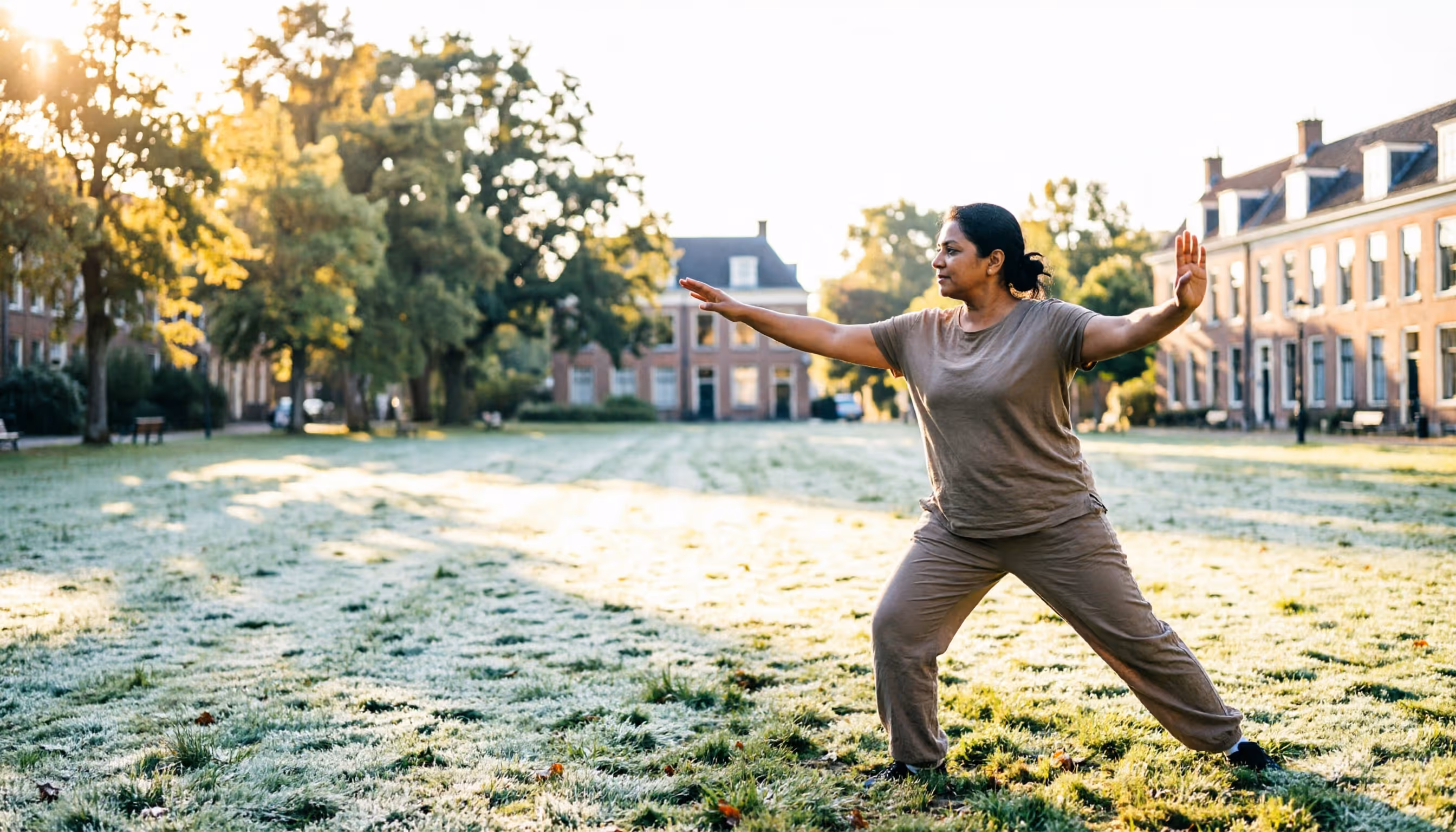 A woman in her early forties moves through a calm tai chi pose in a sunlit Dutch city park in the morning