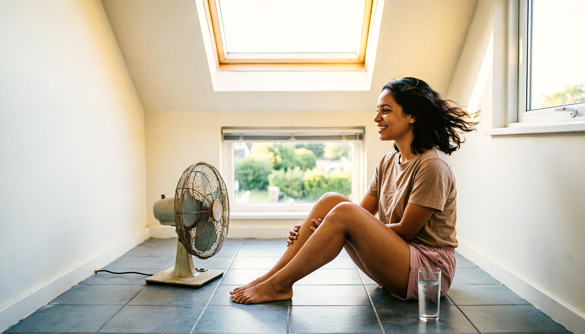 Inkomsten uit overige werkzaamheden uitgelegd: een jonge vrouw koelt af bij een staande ventilator op een Nederlandse zolderkamer op een bewolkte zomermiddag