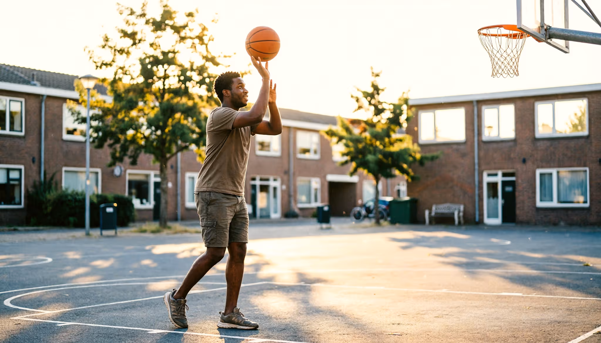 Een jonge man speelt basketbal op een buitenveldje in een Nederlandse stad.