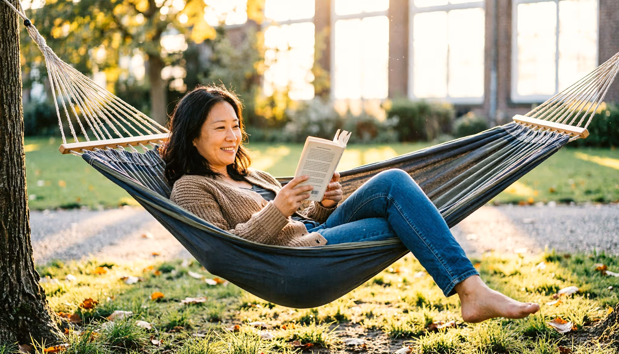 A woman relaxes in a park hammock with a book in the late-afternoon light