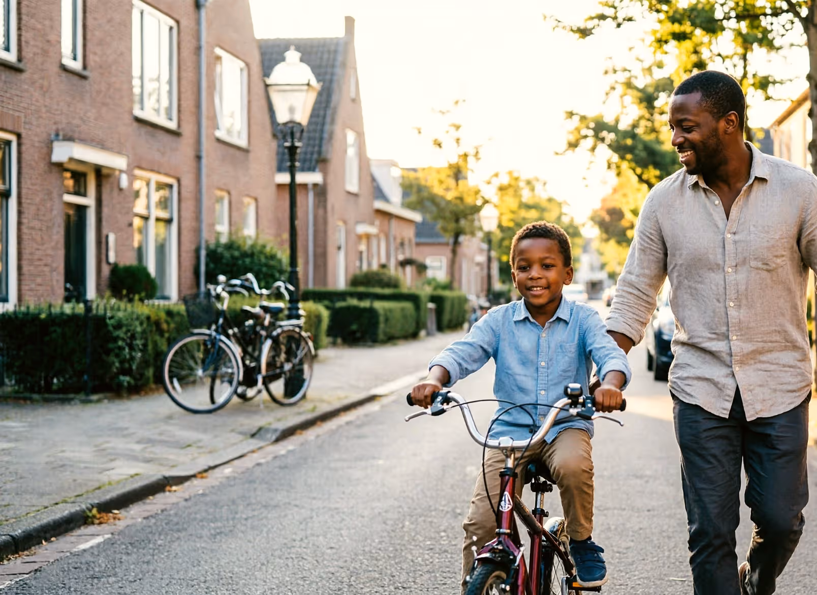 A father runs alongside his young child learning to ride a bike on a quiet Dutch street