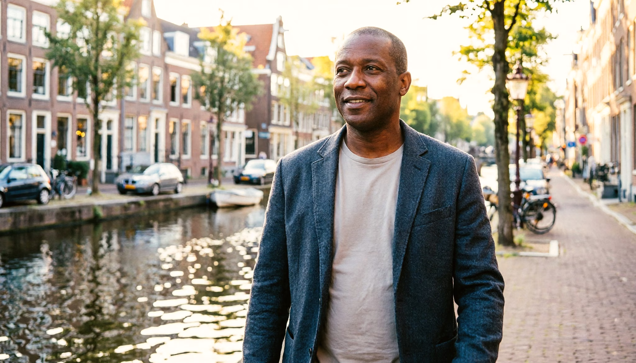 Een man van eind veertig loopt in het ochtendlicht langs een Amsterdamse gracht